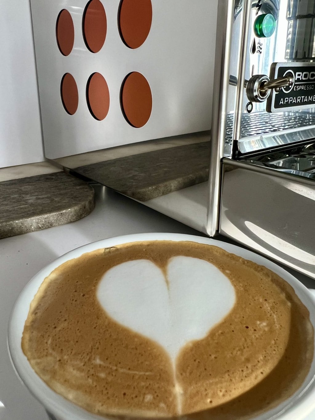 a cup of coffee with a heart on the foam against the background of the Rocket Espresso Appartamento coffee machine