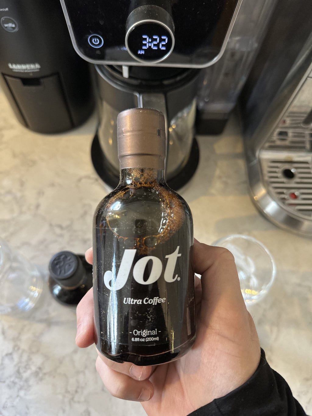 Jot Ultra Coffee in hand against the background of the coffee maker 
