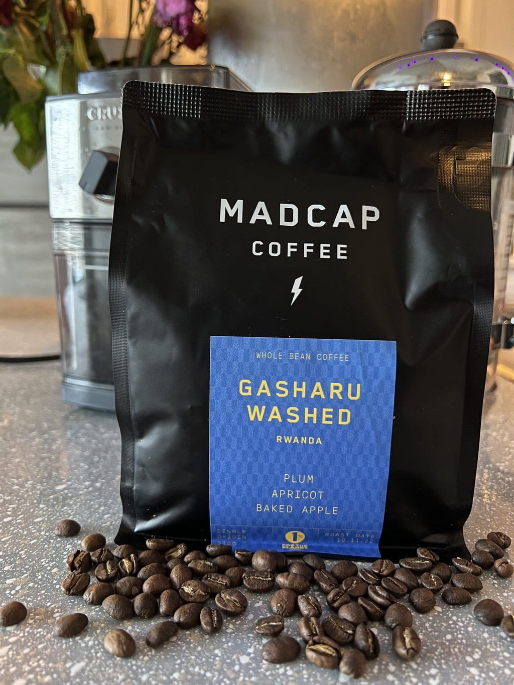 Gasharu Washed - Madcap Coffee pack and scattered coffee beans next to the coffee grinder and french press