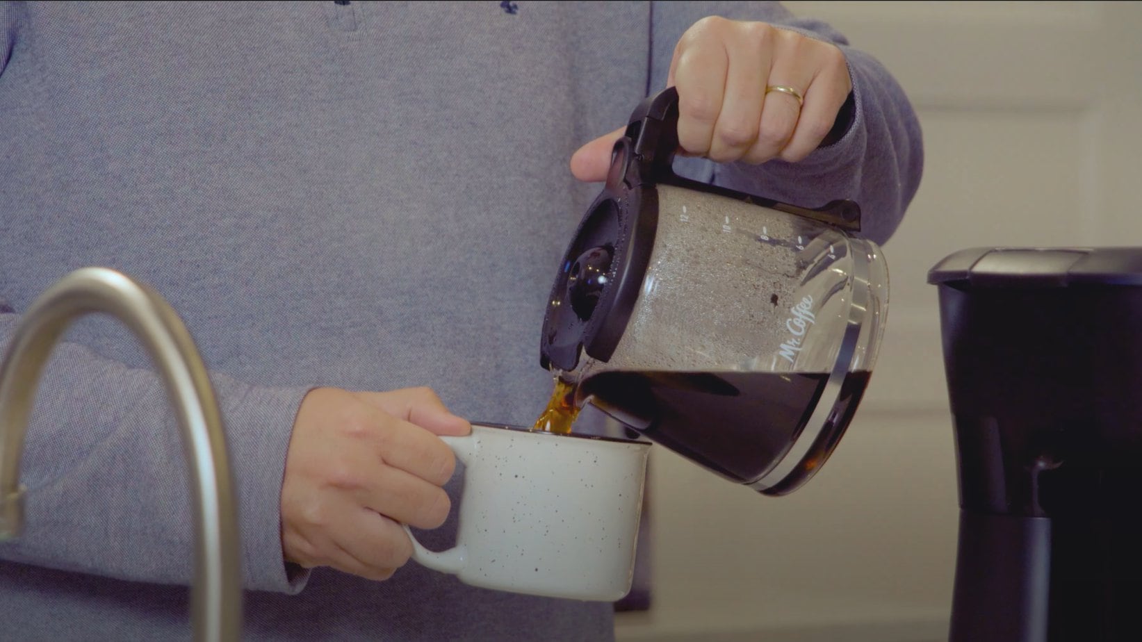 pouring brewed coffee from Roasty's Mr. Coffee carafe into a white coffee mug 