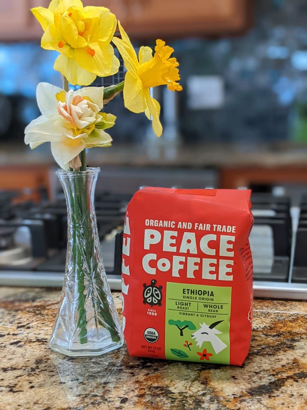 There is a package of Peace Coffee Ethiopia Single Origin Light Roast on the kitchen table, next to a vase with daffodils flowers