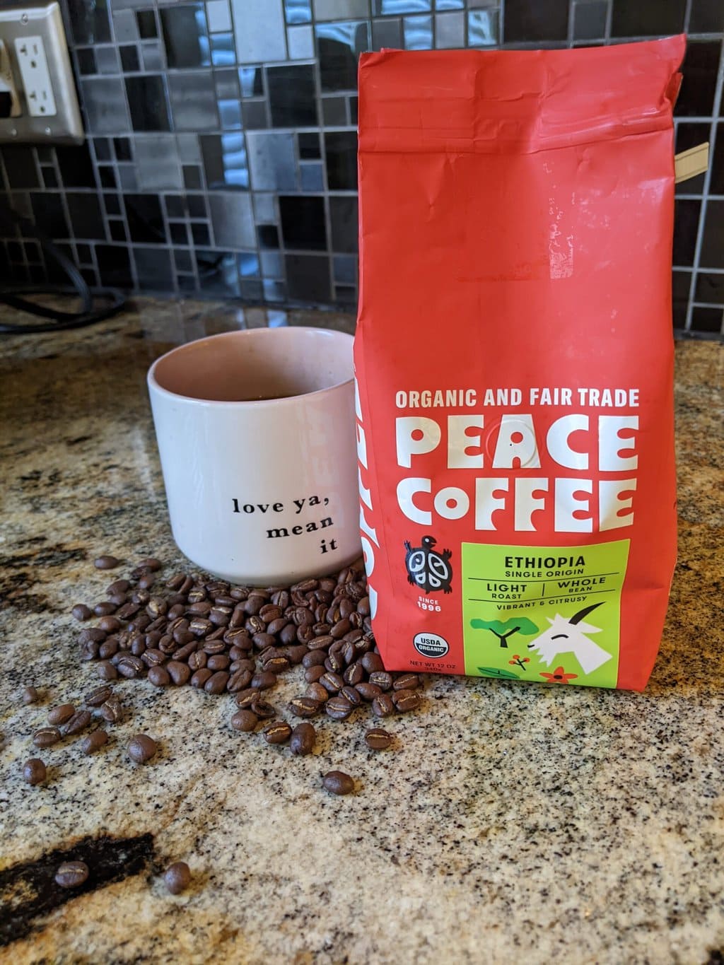 Peace Coffee Ethiopia Single Origin Light Roast next to a brewed cup of coffee and scattered coffee beans