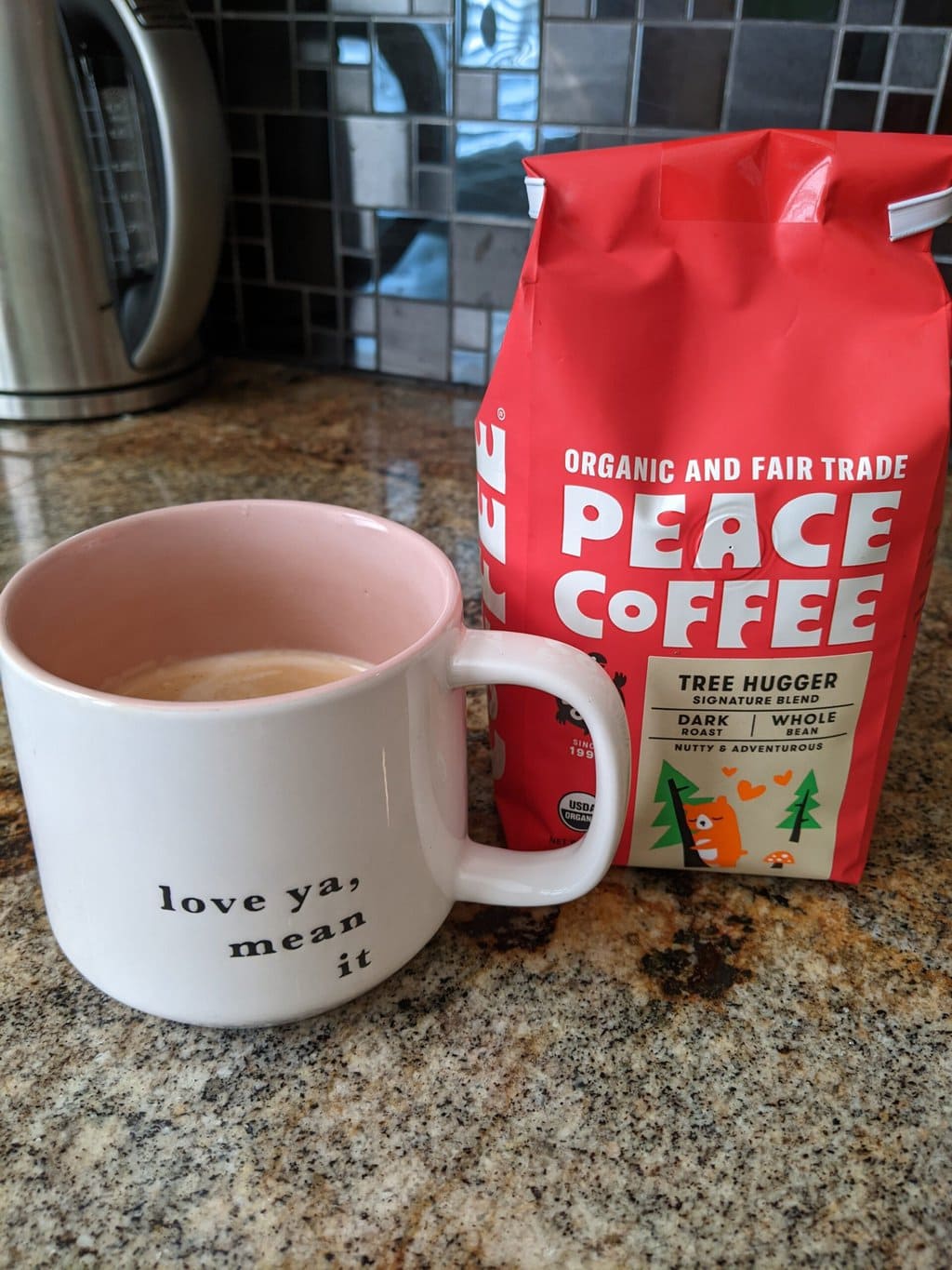 Peace Coffee Tree Hugger Signature Blend Dark Roast stands on the kitchen table next to a brewed cup of coffee