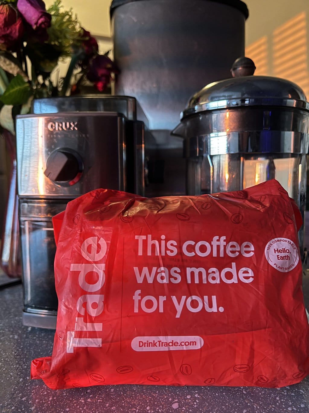 packaging of coffee in a red bag from Trade stands against the background of a coffee grinder and a French press