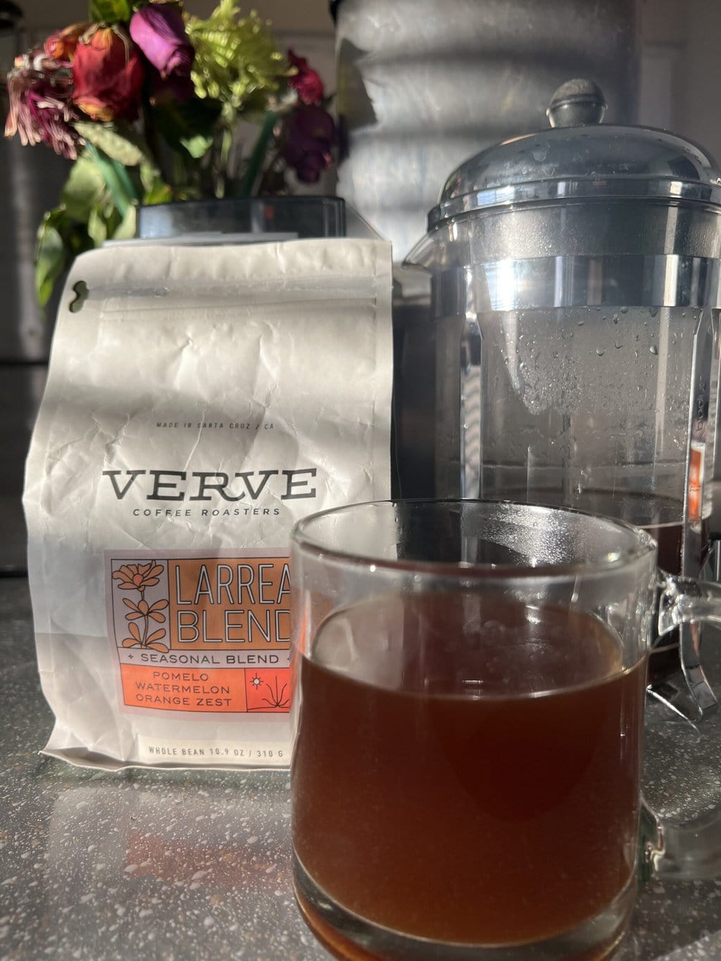 a glass of brewed coffee against the background of Verve Coffee packaging and a French press