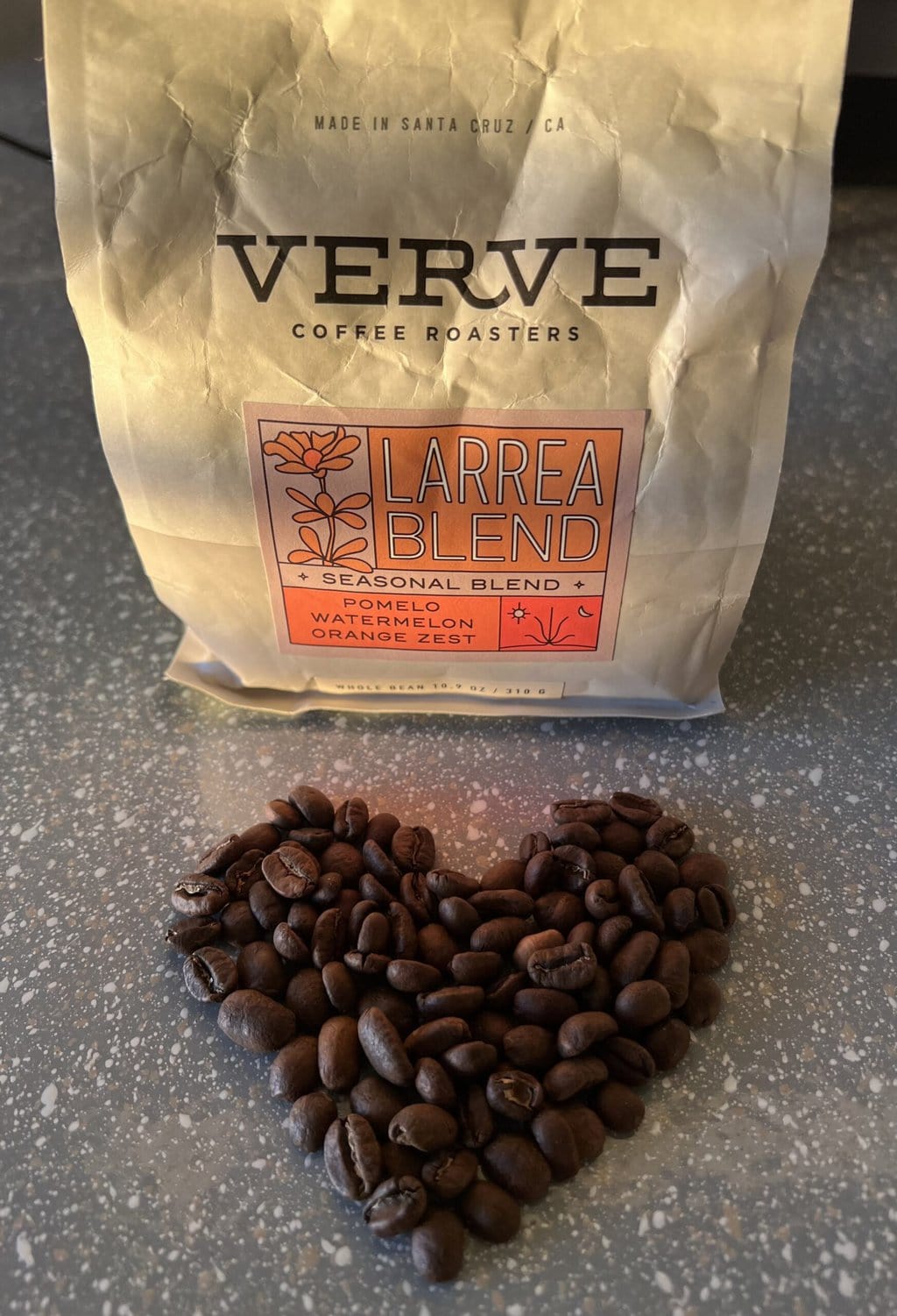 Coffee beans are arranged in a heart shape on a tabletop against the backdrop of Verve Coffee packaging